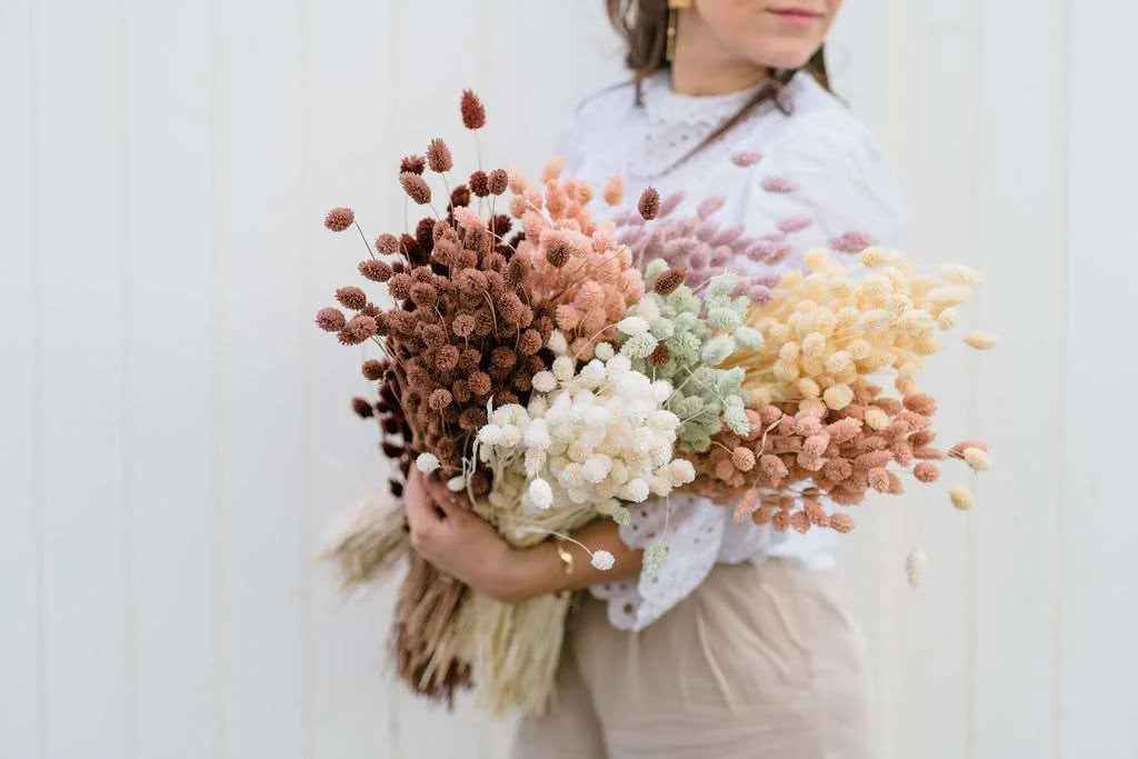 Person holding a bouquet of dried flowers in pink, burgundy, beige and brown tones